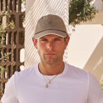 Man wearing a white t-shirt and cap standing outdoors with a neutral background